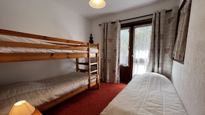 A room with a bunk bed, a single bed, a lamp, and a window with curtains. - VIKING 23 - Village center apartment - Parking (La Clusaz)