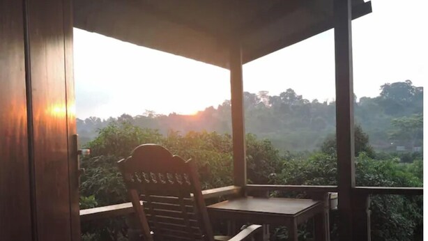 A wooden chair and table on a balcony with a view of a forested area.