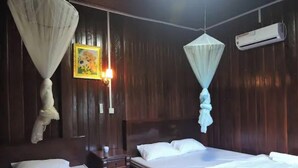 A bedroom with a bed, bedside tables, a nightstand, a wall-mounted air conditioner, and mosquito nets. - Banlung Eco-Lodge Tanam(Mountain View) (Krong Ban Lung)