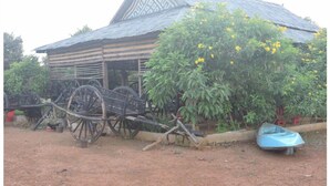 A rustic wooden house with a sloped roof, a wheelbarrow, and a small boat. - Banlung Eco-Lodge Tanam(Mountain View) (Krong Ban Lung)