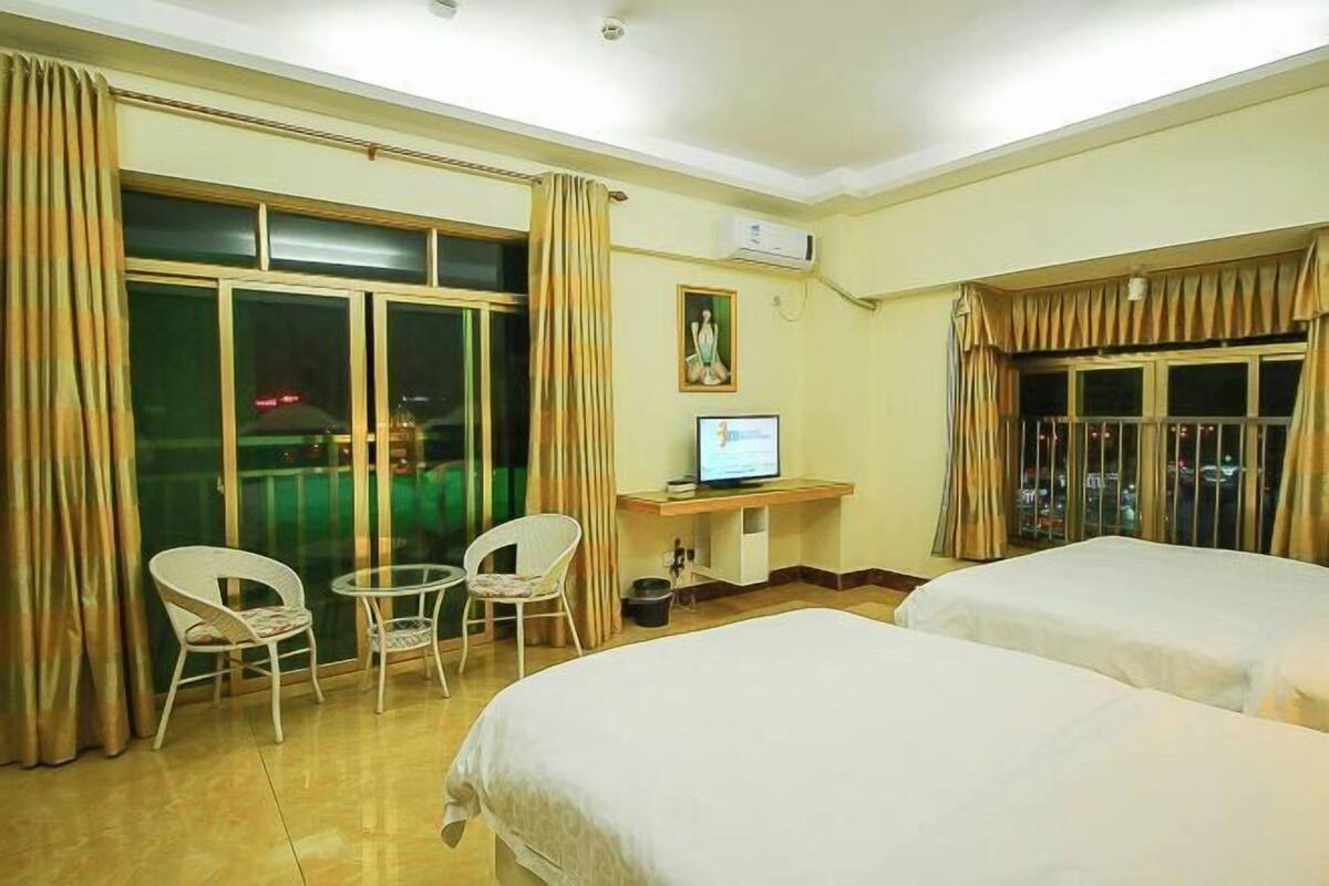 A hotel room with two beds, a desk with a computer, a chair, and a window with curtains.