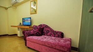 Ένα δωμάτιο με έναν ροζ καναπέ, μια τηλεόραση τοποθετημένη σε ένα έπιπλο και  έναν πίνακα στον τοίχο.