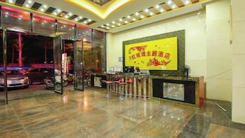 A hotel reception area with a glass entrance, a reception desk, and a large screen displaying text.