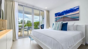 A bedroom with a large bed, a sliding glass door to a balcony, and a painting of a pier at sunset. - Ground floor Oceanfront Studio to Relax and Unwind in Aruba! (Noord)