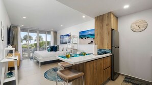 A modern hotel room with a large bed, a kitchenette, a dining area, and a view of palm trees. - Ground floor Oceanfront Studio to Relax and Unwind in Aruba! (Noord)