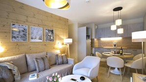 Una sala moderna con un sofá, sillones y un comedor con una mesa y sillas. Hay marcos de cuadros en la pared y una lámpara.