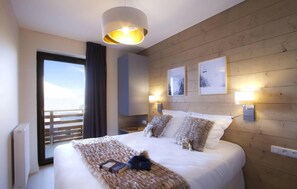 A modern hotel room with a large bed, a view of the sea, wooden paneling, and artwork on the walls. - Wifi, 50m from ski slopes, fitness, swimming pool, sauna, hammam, balcony, parking, tv, ski locker (L'Alpe d'Huez)