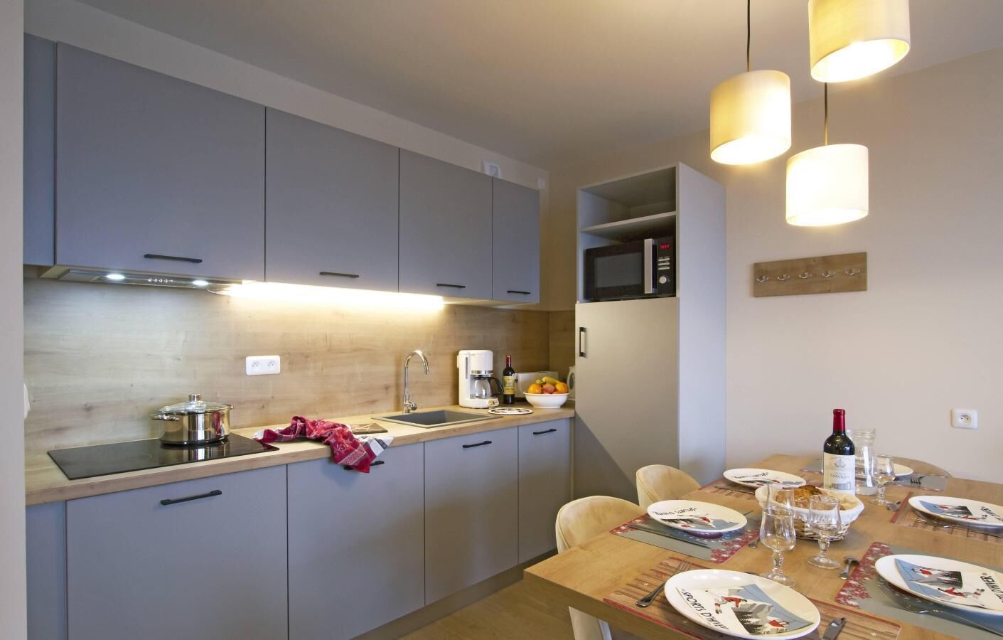 Une cuisine moderne avec des meubles gris, un plan de travail en bois et un coin repas avec une table dressée pour quatre personnes.