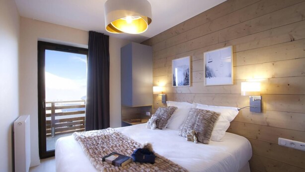 A modern hotel room with a large bed, a view of the sea, wooden paneling, and artwork on the walls. - Wifi, at the foot of shops, fitness, swimming pool, sauna, hammam, balcony, parking, tv, ski locker (L'Alpe d'Huez)