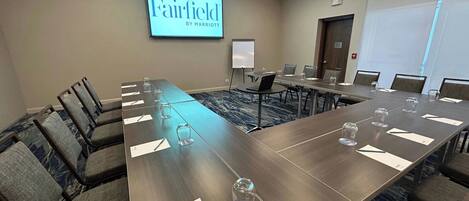 Una sala conferenze con un lungo tavolo, sedie, uno schermo proiettore che mostra "Fairfield by Marriott" e una lavagna.