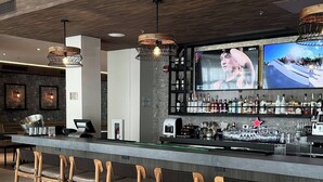 A bar area with wooden chairs, a bar counter, and a large TV screen displaying a movie. - Fairfield by Marriott San Jose Airport Alajuela (Rio Segundo)