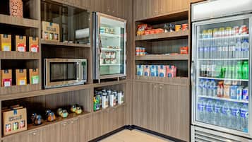 Una kitchenette con microondas, refrigerador y estantes llenos de condimentos y bebidas.