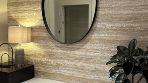 A modern bathroom with a bench, a round mirror, a potted plant, and a wall with a textured pattern. - Fairfield by Marriott San Jose Airport Alajuela (Rio Segundo)