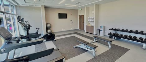 A gym with treadmills, elliptical machines, a bench press, and dumbbells.