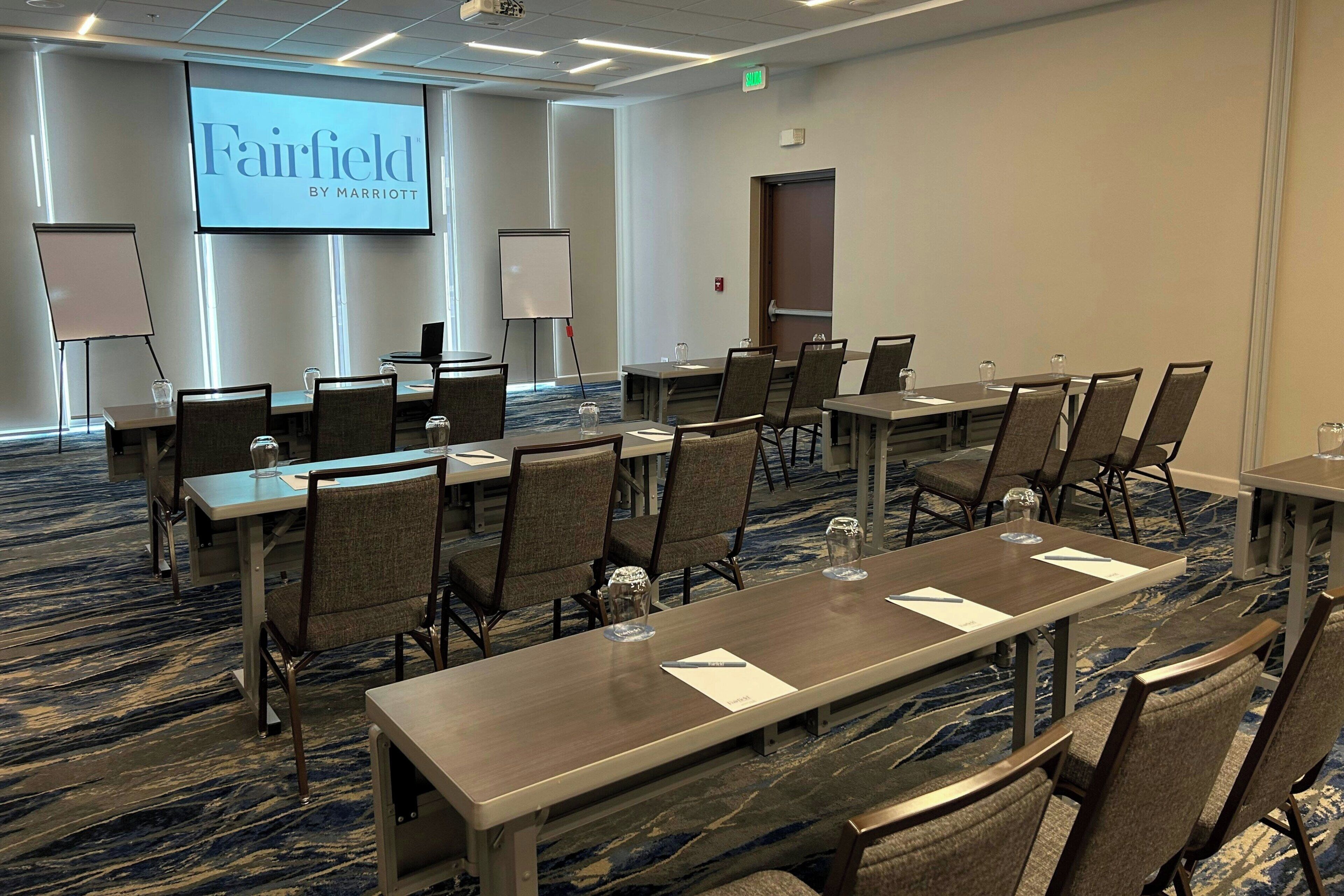 Una sala conferenze con un grande schermo che mostra "Fairfield by Marriott", una lavagna e diversi tavoli con sedie.