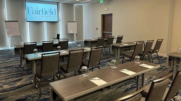 Sala de conferência com uma tela grande exibindo "Fairfield by Marriott", uma lousa e várias mesas com cadeiras.