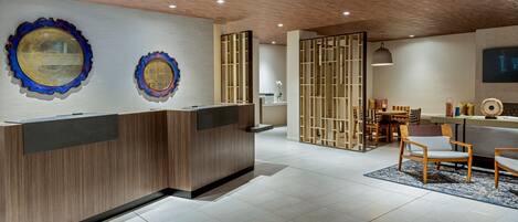 Un espace d’accueil moderne, doté d’un comptoir de réception en bois, de deux miroirs décoratifs et d’un coin salon avec un canapé et des fauteuils.