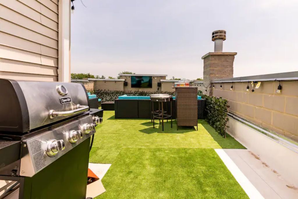 Una terraza en la azotea con césped artificial, una parrilla, mobiliario de exterior y una chimenea.