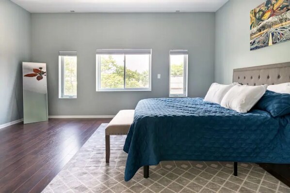 A bedroom with a large bed, two windows, a ceiling fan, and a painting on the wall. - Greystone, 3500 sq ft, Rooftop Access, Sleeps 16 (Chicago)