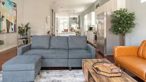 A spacious living room with a grey sectional sofa, a wooden coffee table, and an orange sofa. - Greystone, 3500 sq ft, Rooftop Access, Sleeps 16 (Chicago)