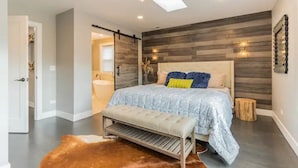 Ein modernes Schlafzimmer mit einem großen Bett, einer Bank, einer Holzvertäfelung und einer Deckenleuchte.