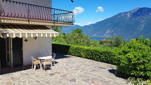 A stone patio with a table and chairs, a balcony with a metal railing, and a view of mountains.