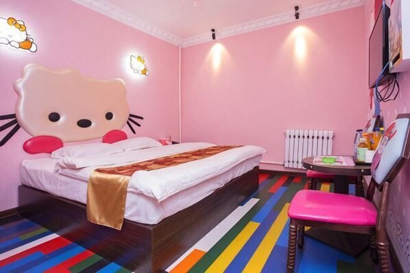 A pink-themed room with a large Hello Kitty bed, a radiator, and a small table with a chair.