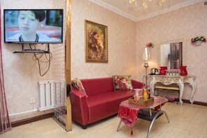 A living room with a red sofa, a TV mounted on the wall, a small table with a lamp, and a decorative mirror.