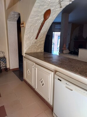 Una cocina con encimera de granito, armarios blancos, una cuchara de madera colgada en la pared y un lavavajillas.