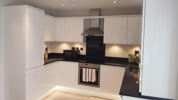 A modern kitchen with white cabinetry, a black countertop, and a built-in oven.