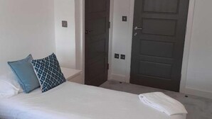 A bedroom with a bed, two doors, and a light switch on the wall.