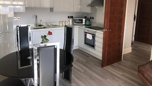 A modern kitchen with white cabinets, a microwave, and an oven. There is a dining table with chairs and a vase with a rose.