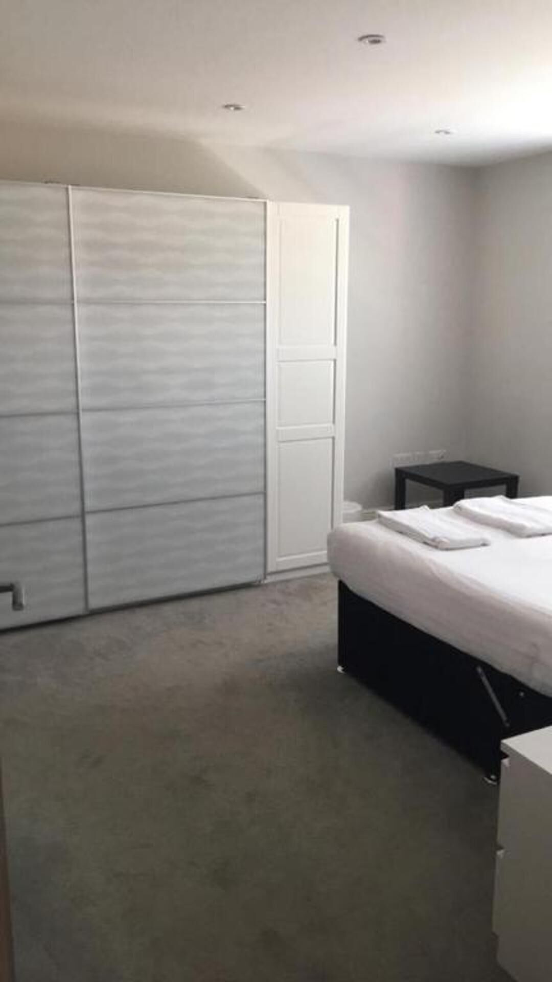 A bedroom with a bed, a small table, and a wardrobe.