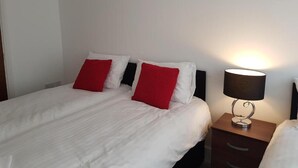A hotel room with a bed, two red pillows, a white duvet, and a bedside lamp.