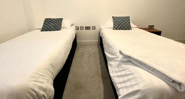 A hotel room with two single beds, each with a patterned pillow and a small bedside table. - Lovely 2-bed Apartment in Brentwood (Brentwood)