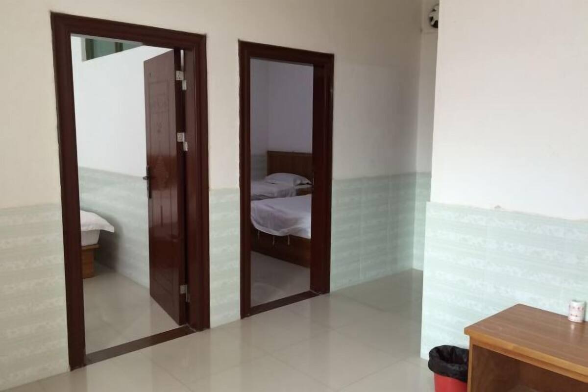 A room with a bed, a wooden table, and a trash bin.