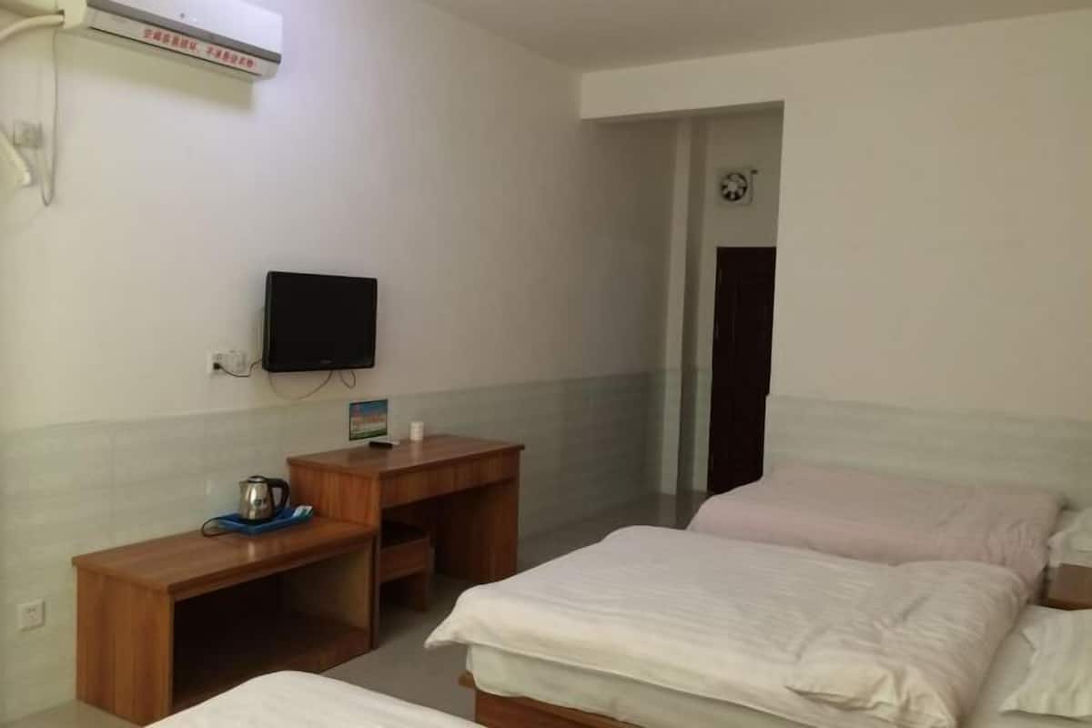 A hotel room with two beds, a TV, a wooden desk, and a small table with a kettle.