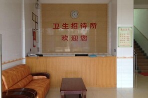 A reception area with a wooden reception desk, a clock, and a sign with text. - Weisheng Hostel (Xinfeng)