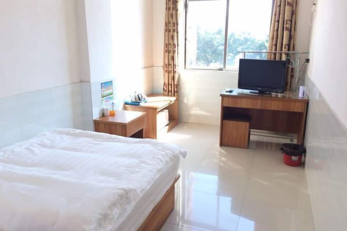 A hotel room with a bed, a desk with a computer, a television, and a window with curtains.