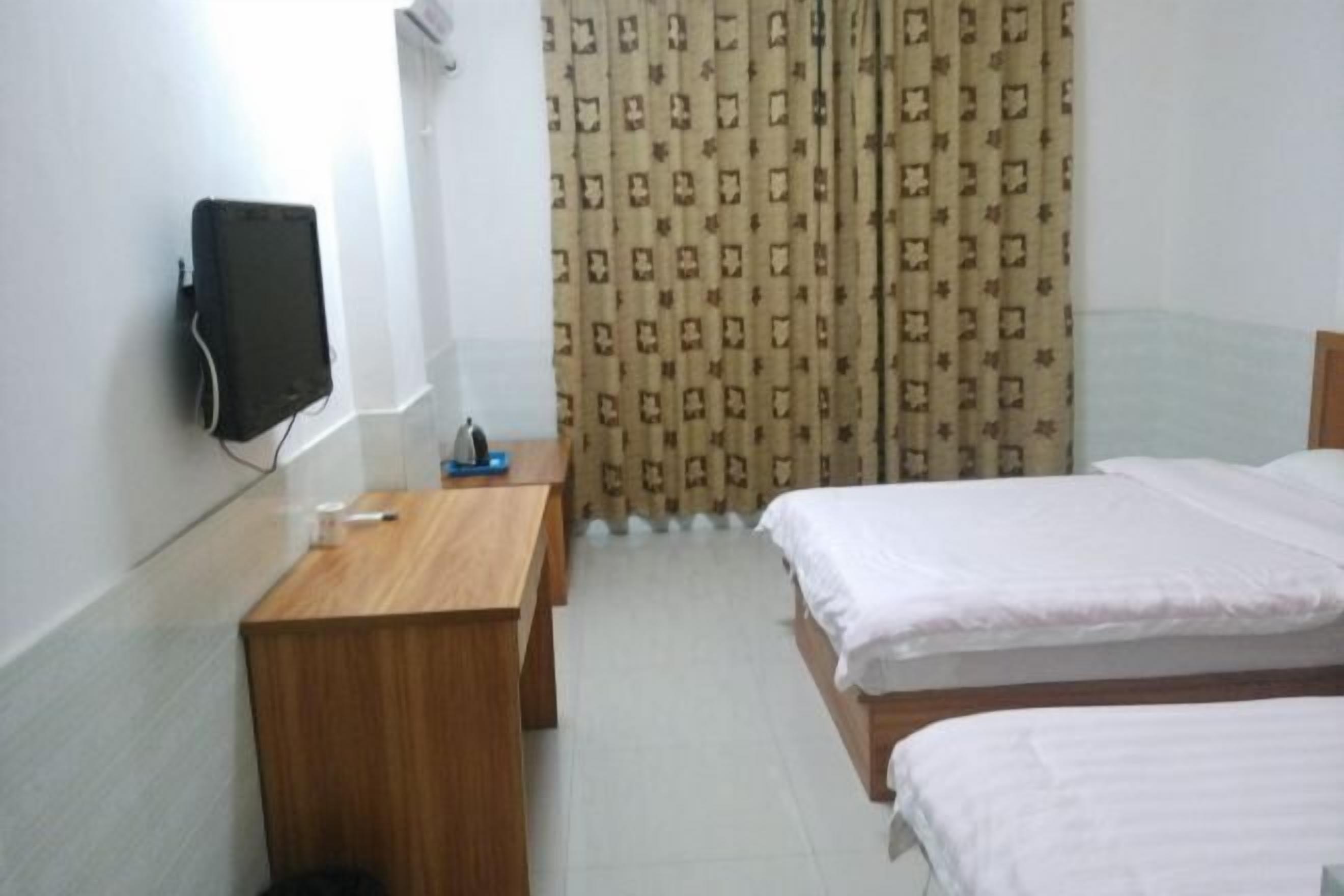 Een hotelkamer met een houten bureau, twee bedden, een aan de muur bevestigde televisie en kamerbreed gordijn.
