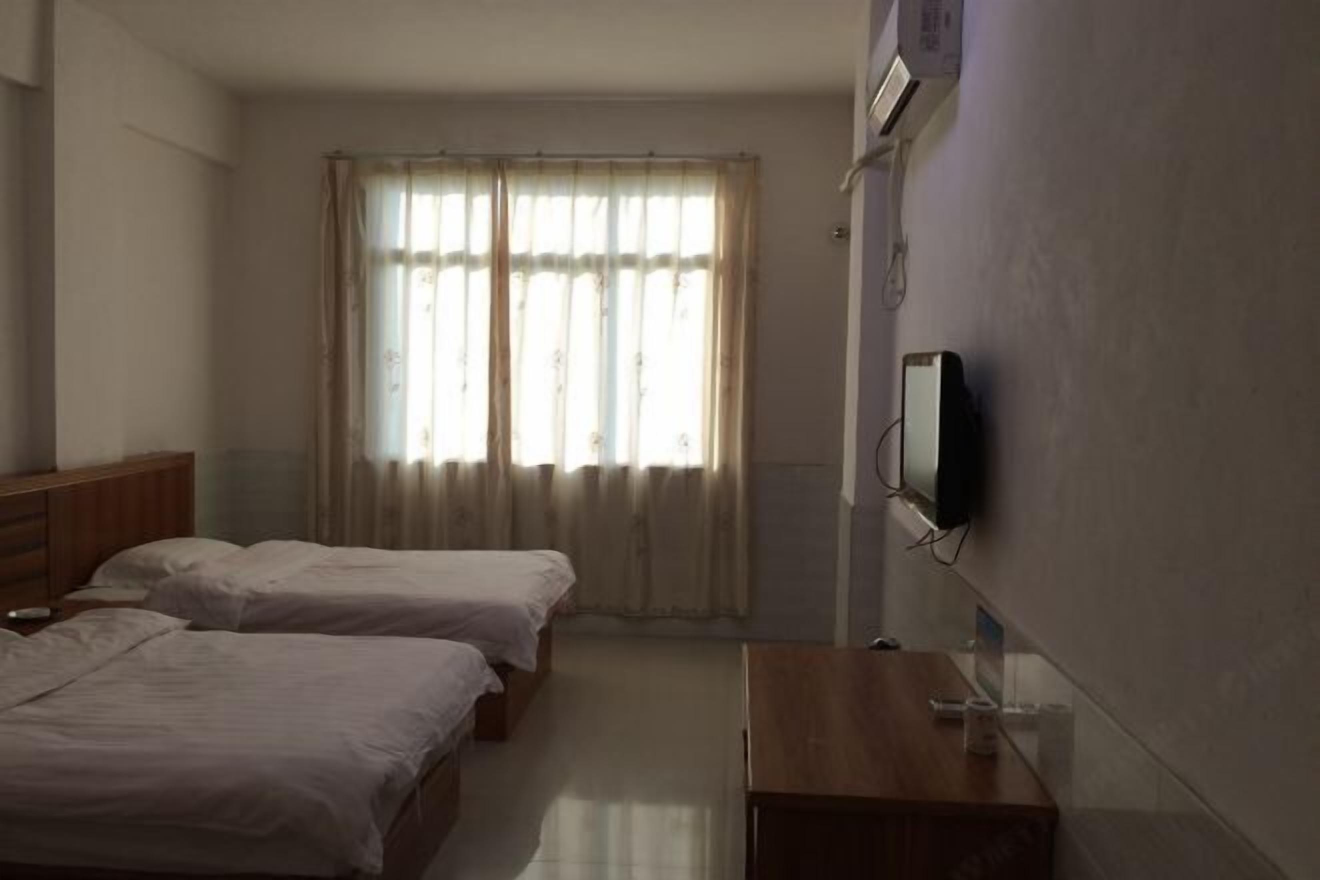 Een hotelkamer met twee bedden, een houten dressoir, een aan de muur bevestigde televisie en een raam met gordijnen.