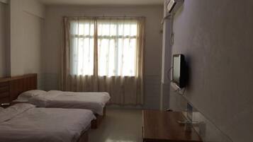 Een hotelkamer met twee bedden, een houten dressoir, een aan de muur bevestigde televisie en een raam met gordijnen.