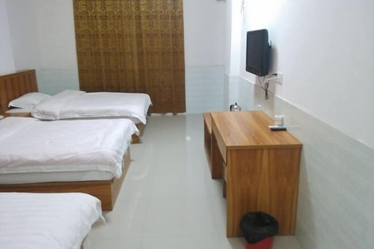 A hotel room with two single beds, a wooden desk, a television mounted on the wall, and a curtain.