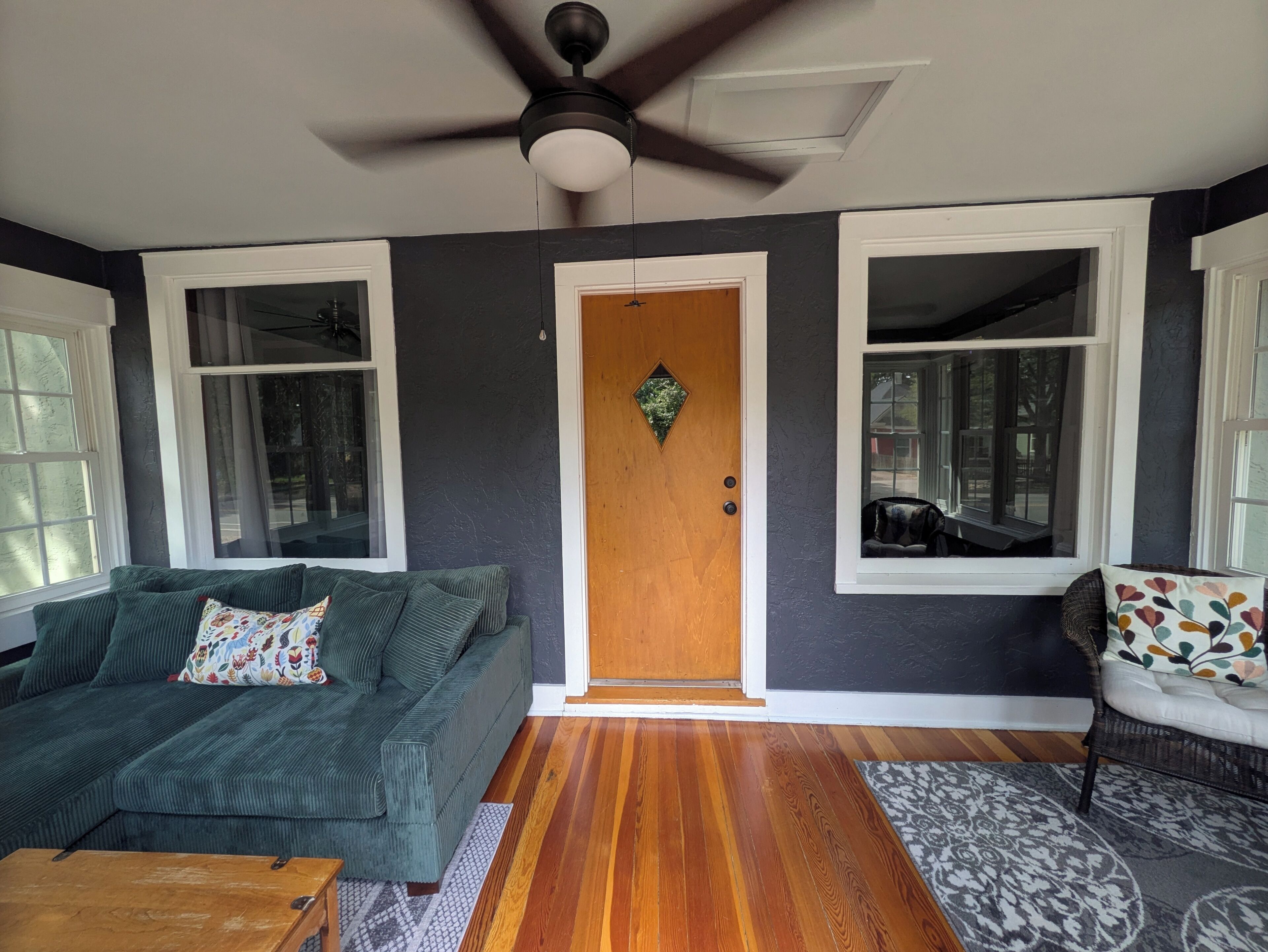Uma sala de estar com um sofá verde, uma mesa de centro de madeira, um tapete estampado e uma porta de madeira com um vitral.