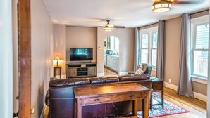A living room with a brown leather sofa, a wooden coffee table, a TV, and a ceiling fan.
