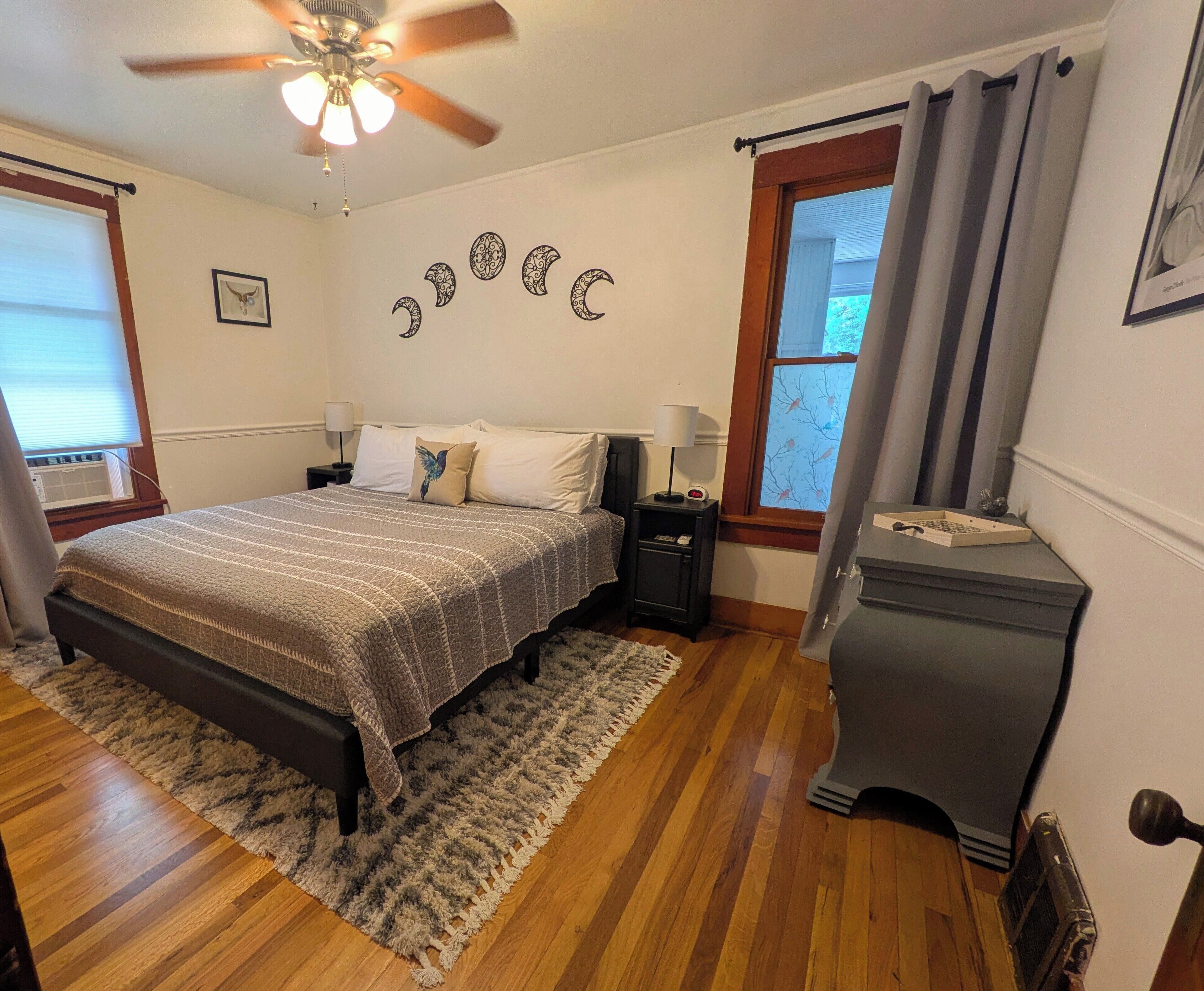 A bedroom with a bed, nightstands, a dresser, a ceiling fan, and a window with curtains.