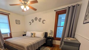 A bedroom with a bed, nightstands, a dresser, a ceiling fan, and a window with curtains.