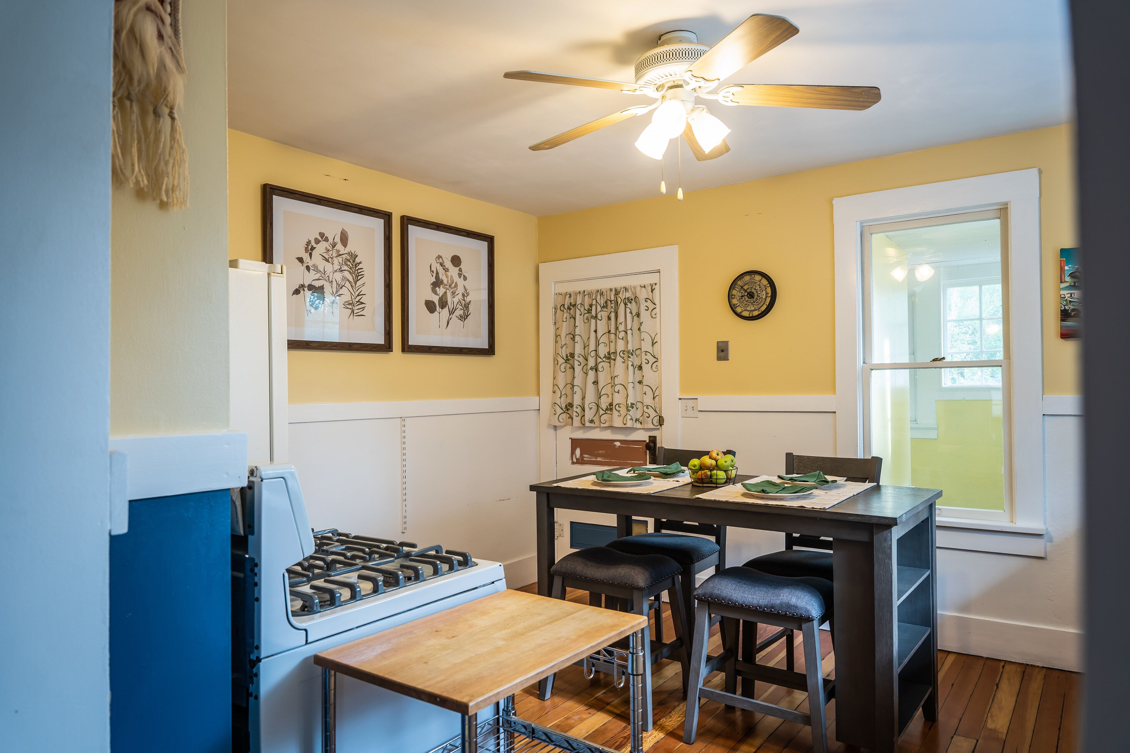 Une cuisine équipée d’une cuisinière, d’une table à manger avec quatre chaises, d’un ventilateur de plafond et d’une fenêtre donnant sur un beau paysage.