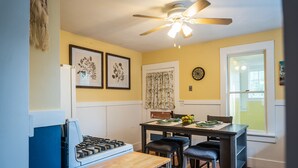 A kitchen with a stove, a dining table with four chairs, a ceiling fan, and a window with a view.