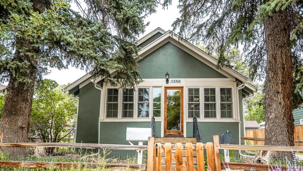 A small, green building with a wooden porch and a mailbox.